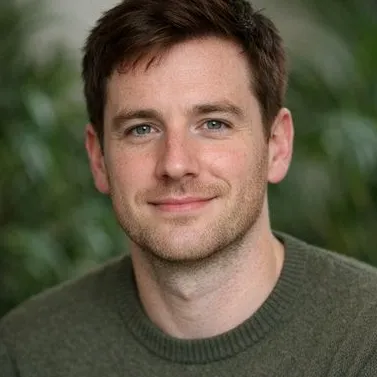Man in his early thirties, dark auburn hair, grey-green eyes, olive knit sweater
